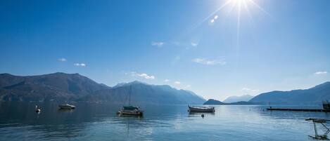 A wooden dock extending into calm water with boats anchored nearby and mountains in the background.