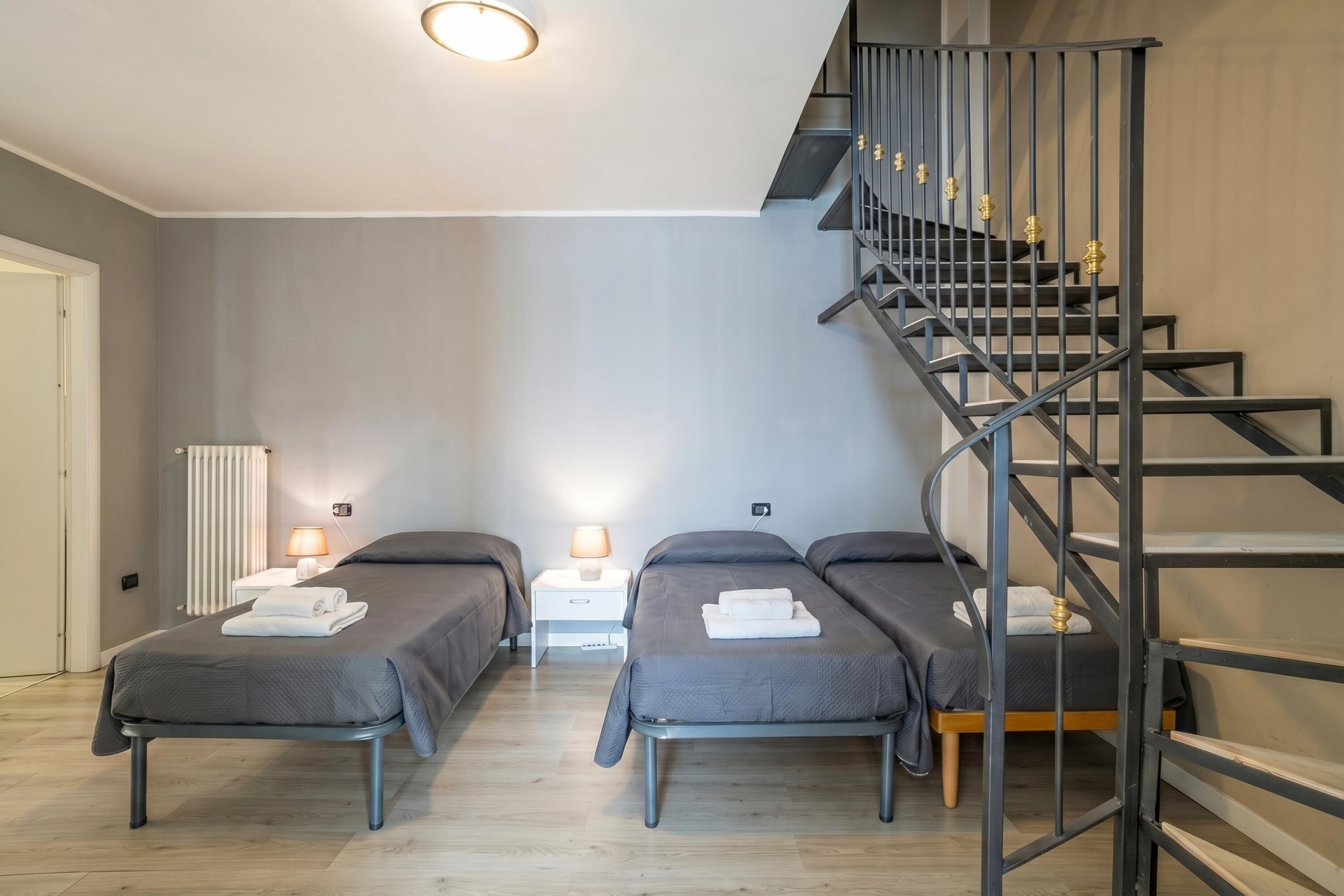 Habitación de hotel con dos camas individuales, una escalera, un radiador blanco y lámparas de noche.