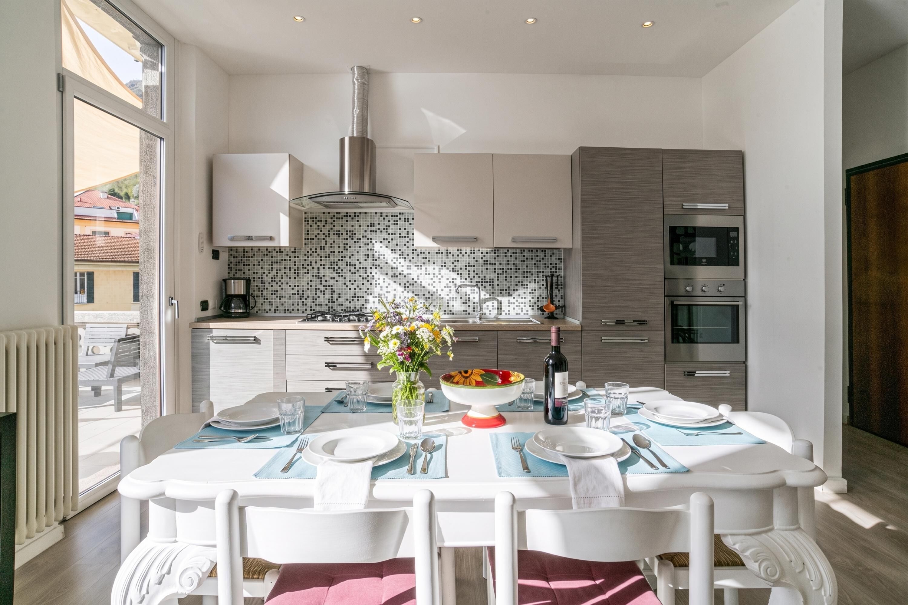 A modern kitchen with white cabinets, a tiled backsplash, and a dining area with a table set for two.