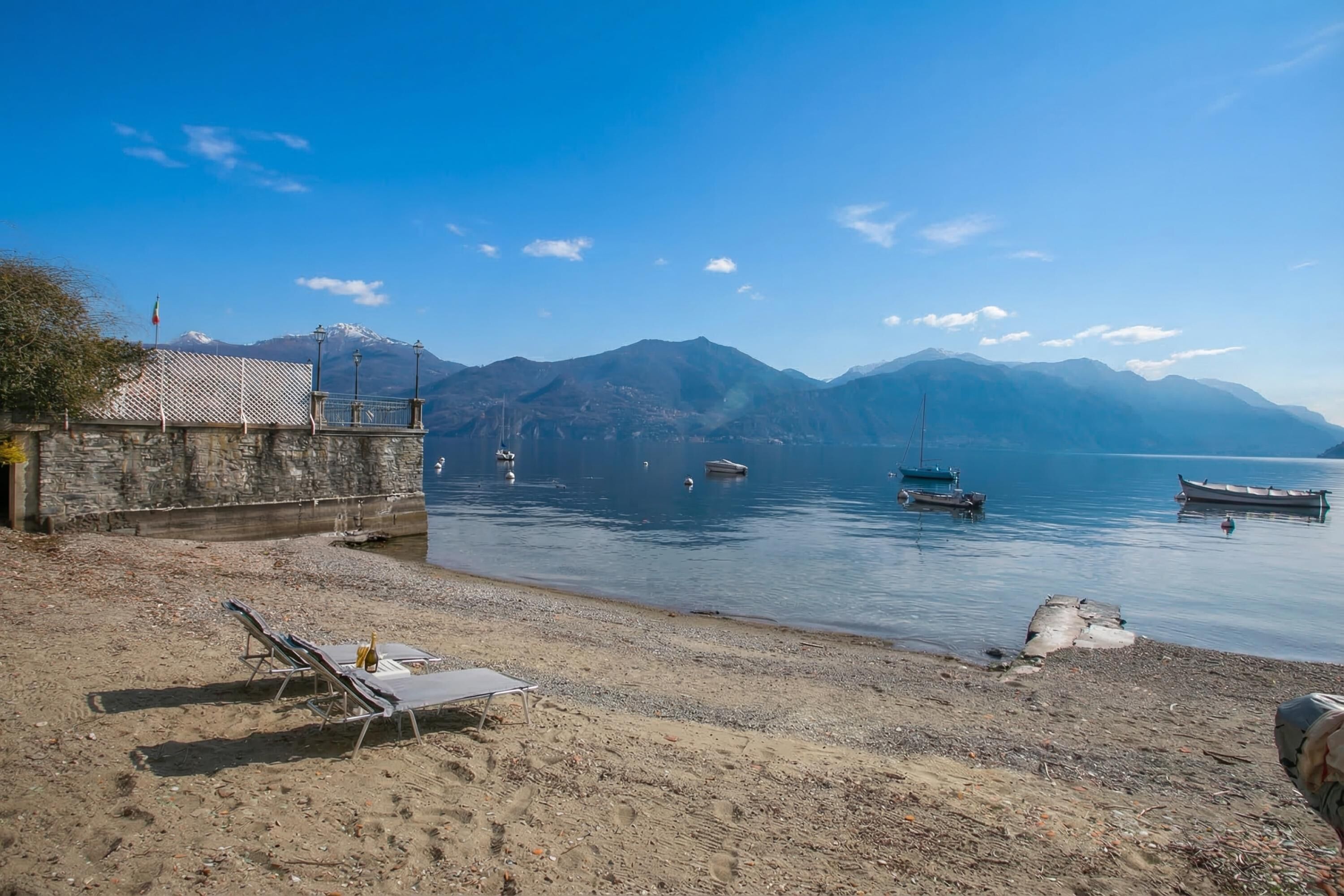 Une plage avec des chaises longues, un bâtiment en pierre et des bateaux sur l’eau.