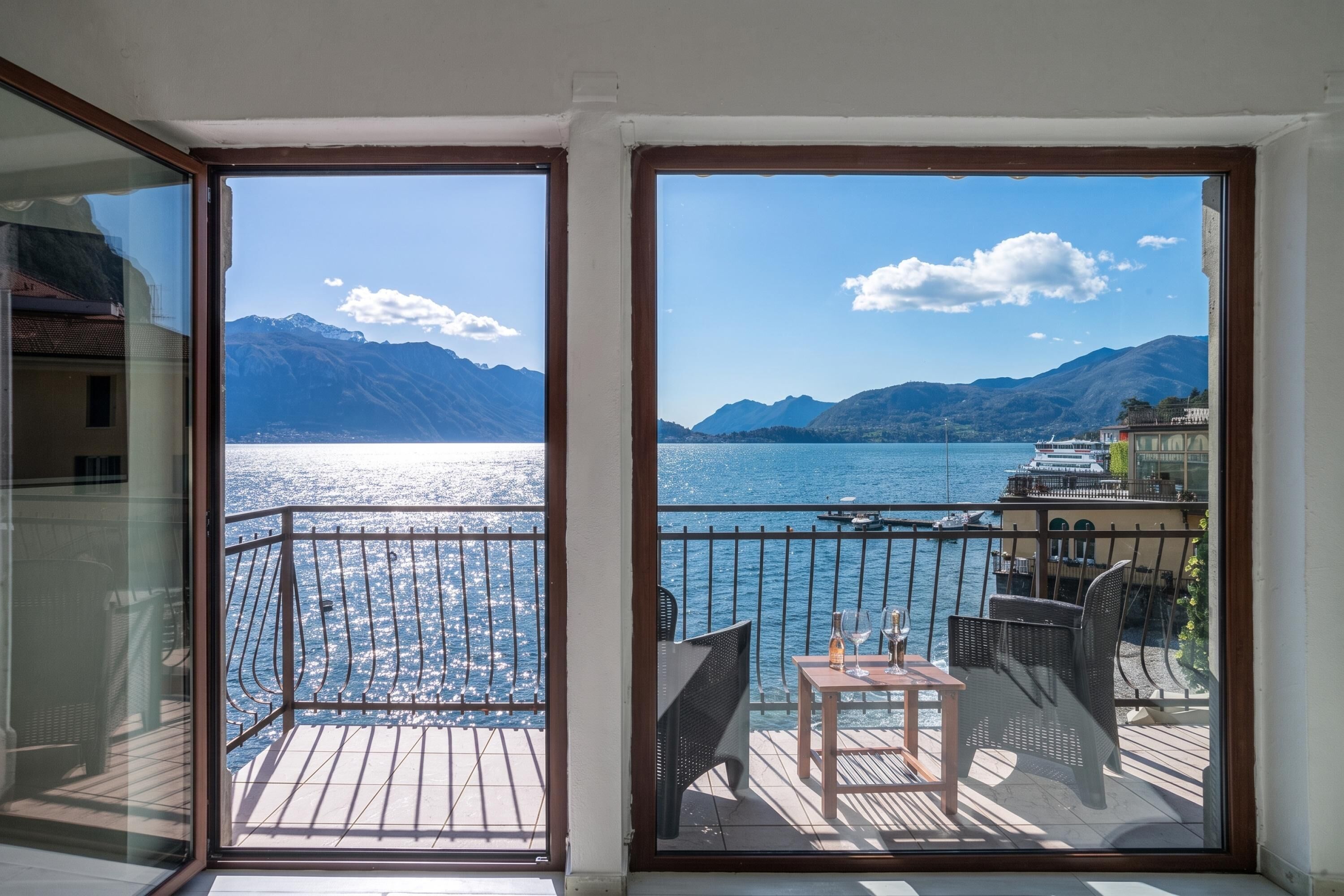 A balcony with a view of a lake and mountains, furnished with chairs and a table.