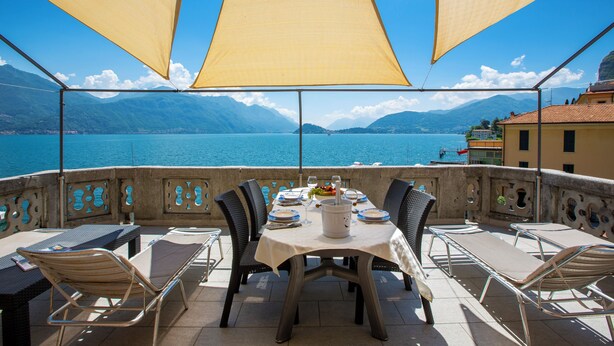 A terrace with a table set for dining, overlooking a lake with mountains in the background. - Menaggio Tosca Apartments (Menaggio)