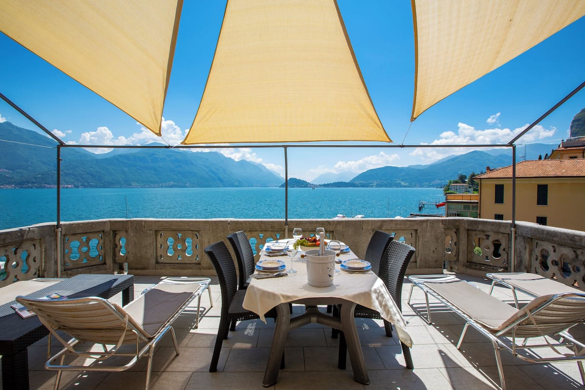 A terrace with a table set for dining, overlooking a lake with mountains in the background.