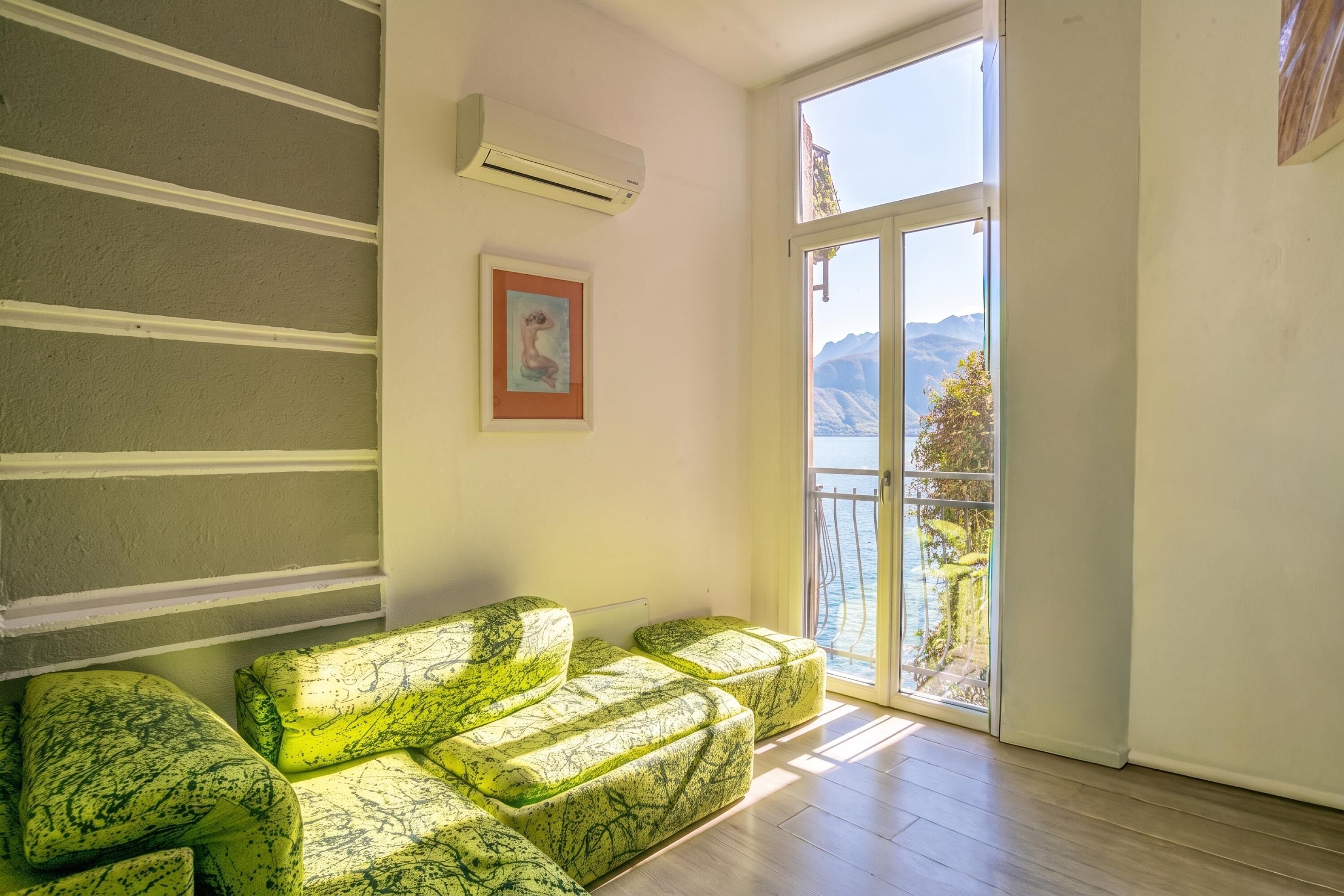 Habitación con sofá, aire acondicionado, un cuadro enmarcado y vistas a las montañas a través de un ventanal.