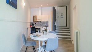 A dining area with a round table, four chairs, a book, and a bottle of champagne. A kitchen is visible in the background. - Menaggio Tosca Apartments (Menaggio)