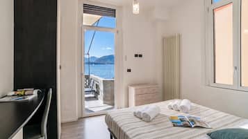Een slaapkamer met een bed, een bureau, een dressoir en uitzicht op zee.