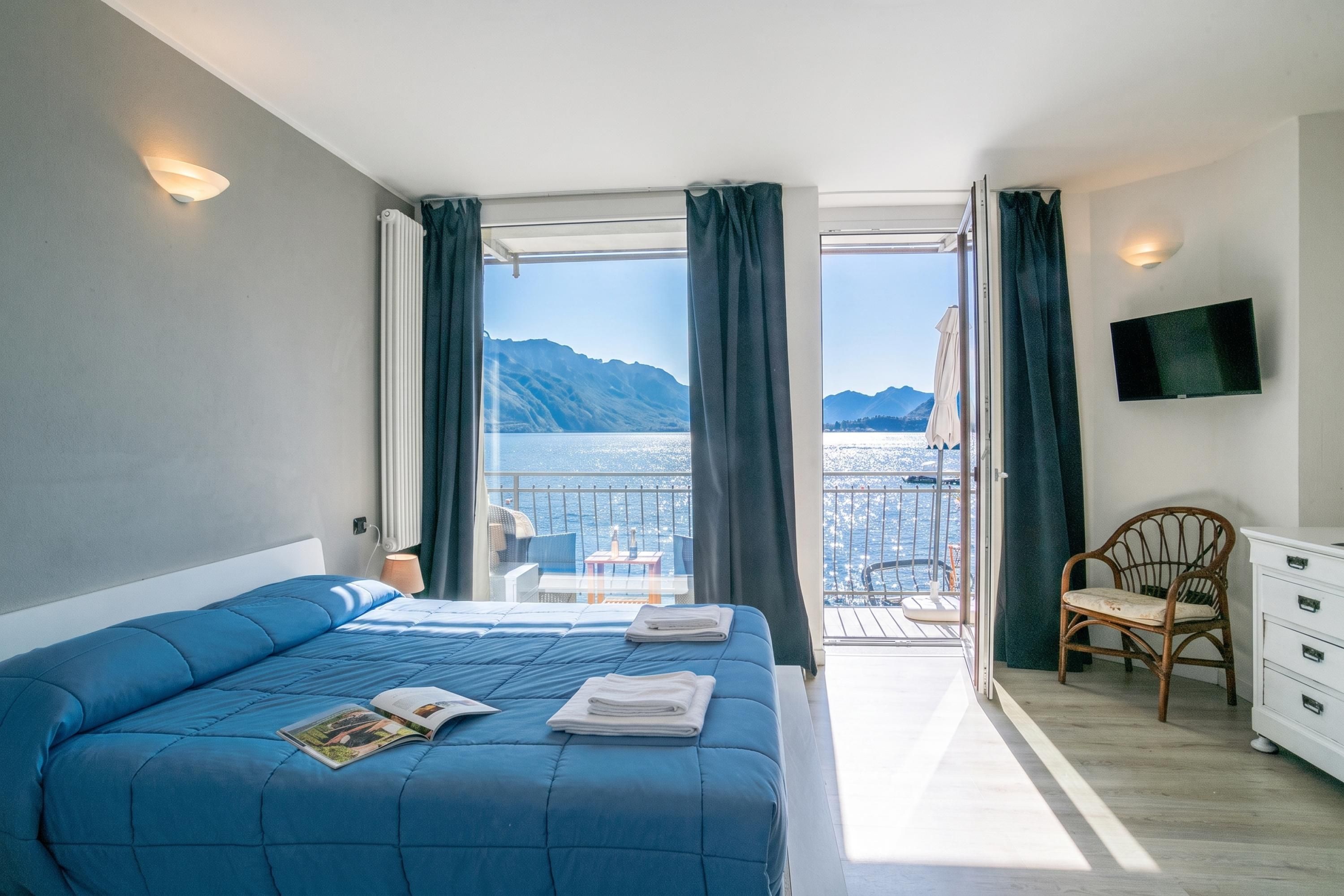 Un dormitorio con una cama grande, un televisor montado en la pared y un balcón con vistas al mar y a las montañas.