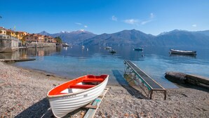 A boat docked at a pebbled shore with a clear view of mountains in the background. - Menaggio Tosca Apartments (Menaggio)