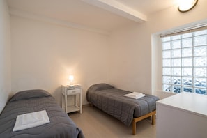 A small, clean room with two beds, a bedside table with a lamp, and a window with a view of snow outside. - Menaggio Tosca 2 (Menaggio)