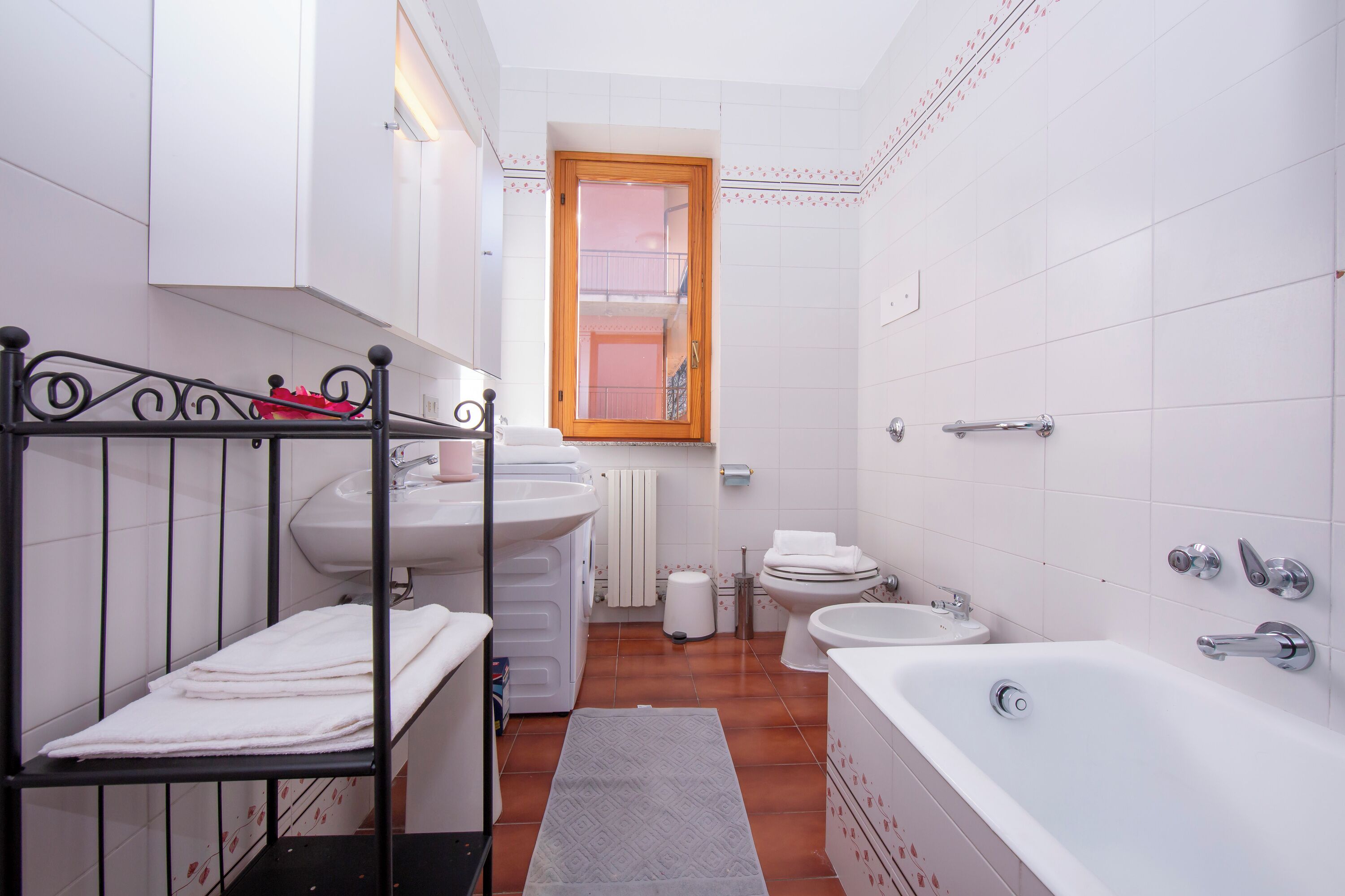 A compact bathroom with a bathtub, two sinks, a toilet, and a window.
