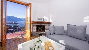 Un salon avec un canapé, une cheminée, un balcon doté d’une table et de chaises, et une vue sur les montagnes.