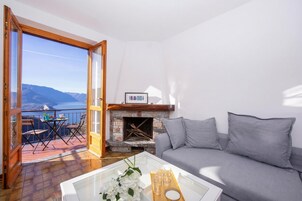 A living room with a sofa, a fireplace, a balcony with a table and chairs, and a view of the mountains.