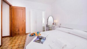 Une chambre d’hôtel avec une porte en bois, une armoire blanche, un lit avec du linge de lit blanc, une table de chevet avec une lampe et un magazine sur le lit.