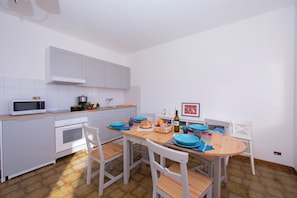 Una cocina con armarios blancos, microondas, estufa y una mesa de comedor con sillas.