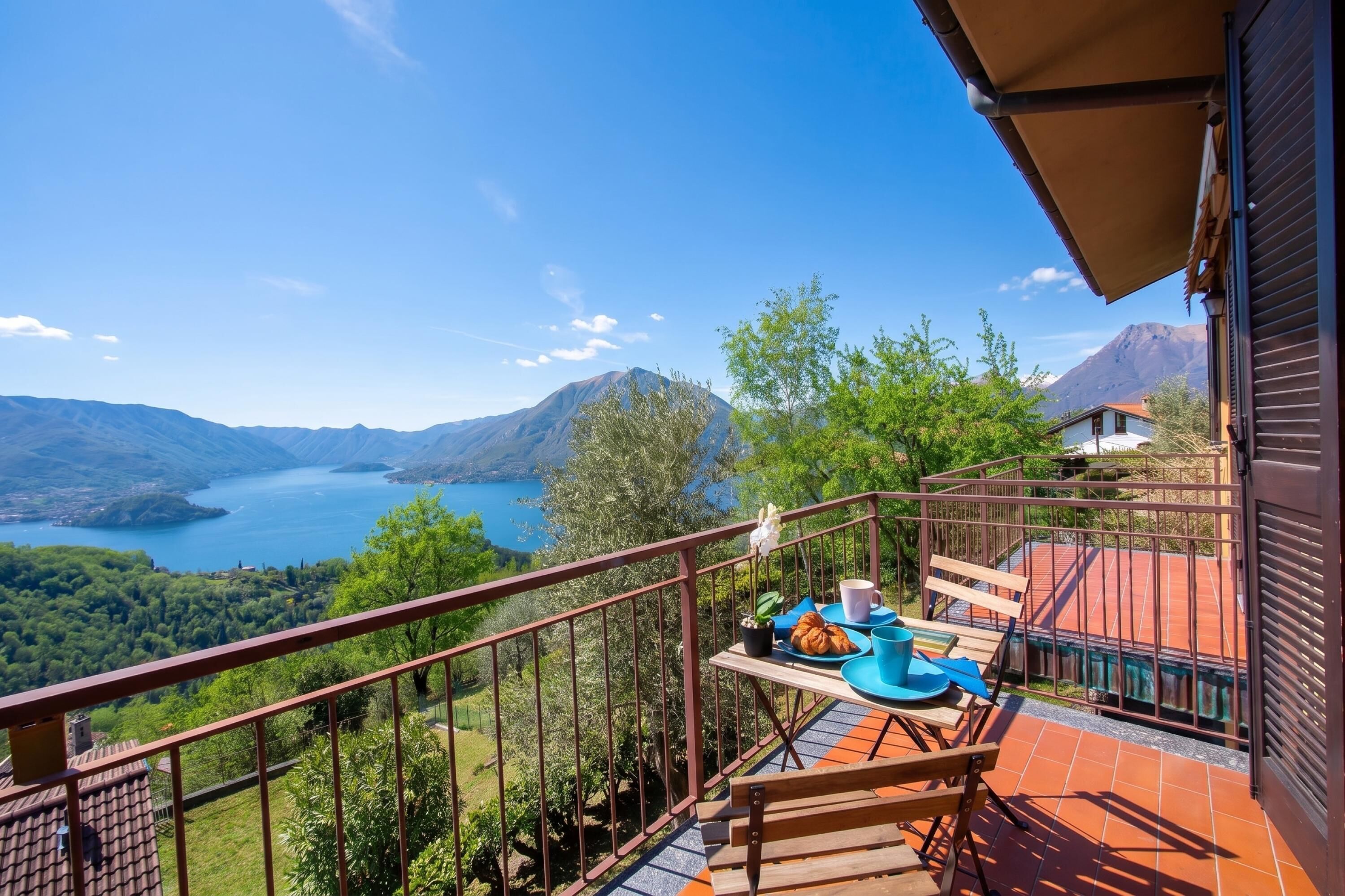 Un balcon avec une table préparée pour le petit-déjeuner, offrant une vue sur un lac et des montagnes.