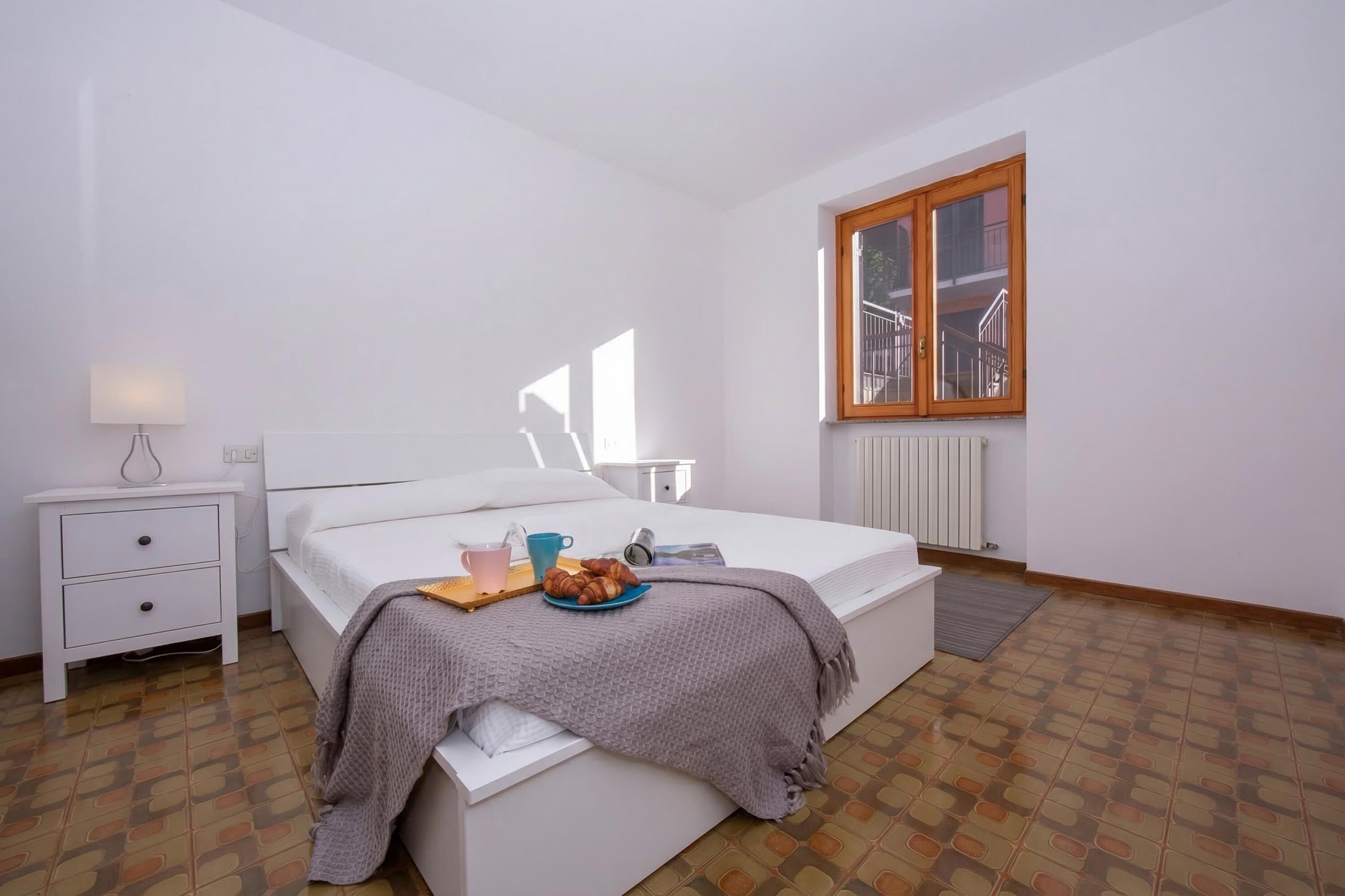 A bedroom with a bed, bedside table, lamp, and a window with a view.