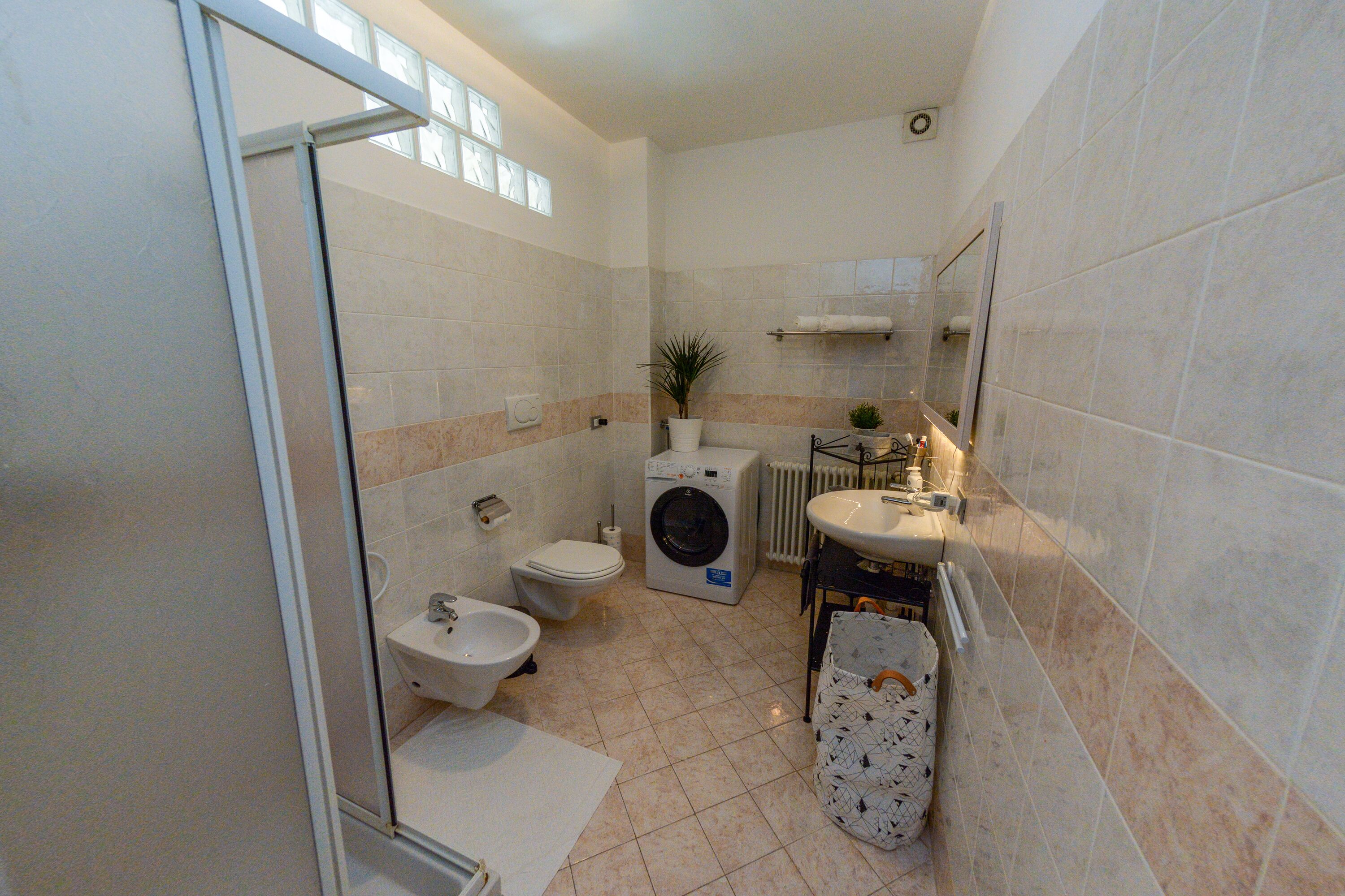 Een kleine badkamer met toilet, bidet, wasmachine en wastafel.