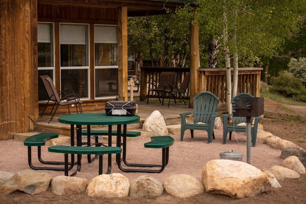 Una cabaña rústica con terraza de madera, asientos exteriores y mesas de picnic.