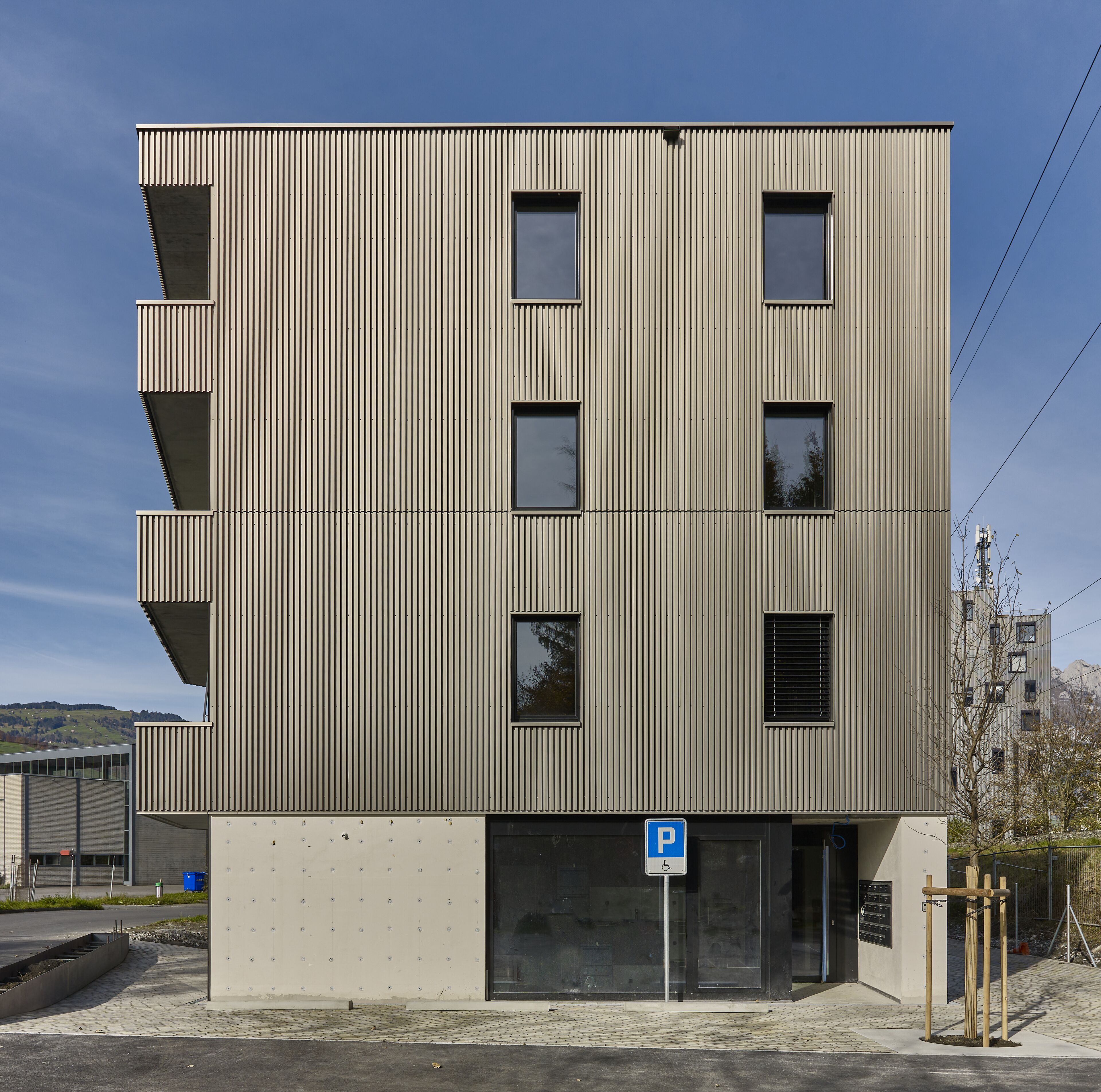 Ein modernes mehrstöckiges Gebäude mit einer wellenförmigen Metallfassade, einem Parkschild und einem befahrbaren Eingangstor.