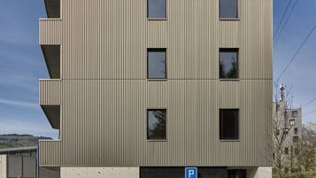 Ein modernes mehrstöckiges Gebäude mit einer wellenförmigen Metallfassade, einem Parkschild und einem befahrbaren Eingangstor.