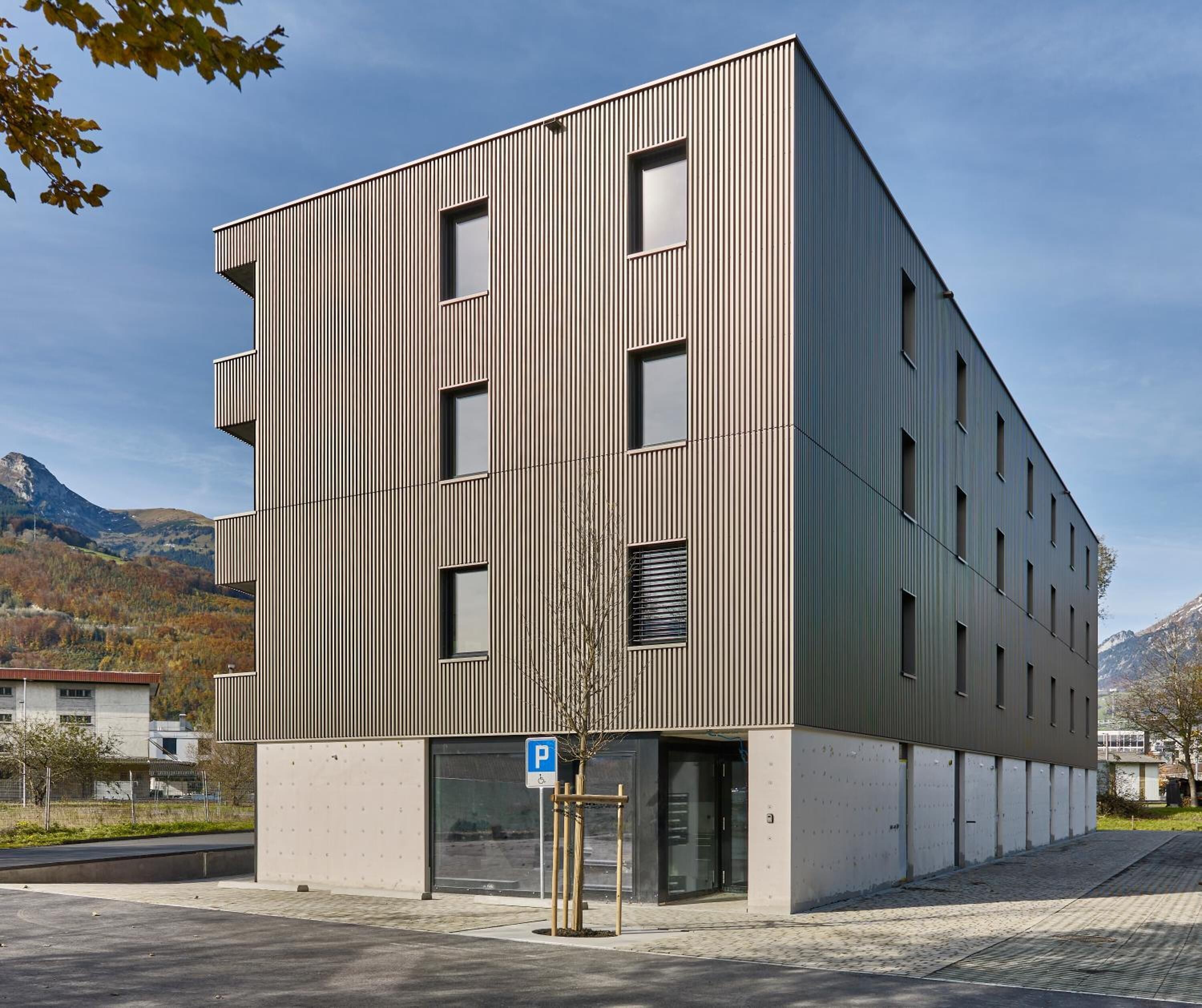 A modern multi-story building with a vertical ribbed facade, a parking sign, and a clear view of the surrounding landscape.