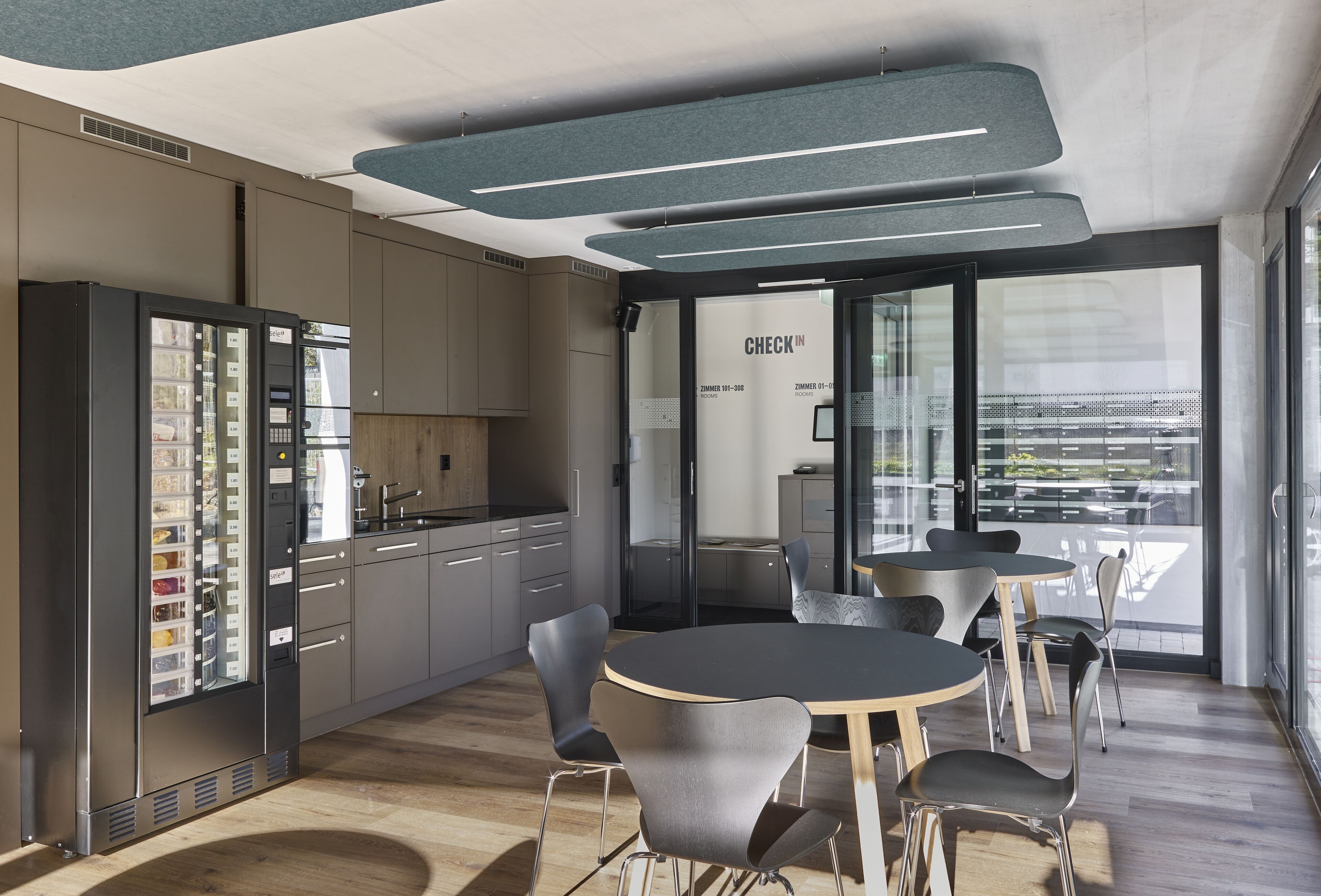 Une cuisine moderne dotée d’un réfrigérateur encastré, un coin repas avec des tables et des chaises rondes, et un comptoir d’accueil avec une porte en verre.