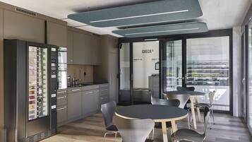 A modern kitchen with a built-in refrigerator, a dining area with round tables and chairs, and a check-in counter with a glass door.