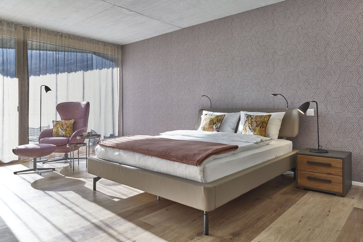 Une chambre moderne avec un grand lit, une chaise, des tables de chevet et un mur décoré d’un motif.