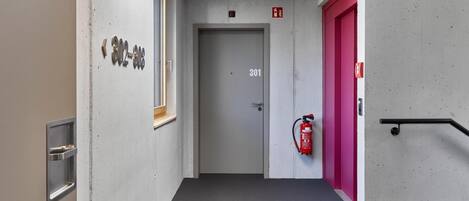 Un pasillo con un extintor, una puerta con la leyenda '301' y un ventanal con vistas al cielo.