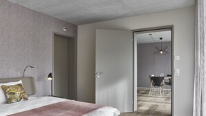 A modern hotel room with a bed, bedside lamps, a door leading to a dining area, and a patterned wall. - BoHo by Maier - kontaktloser Check-In (Buchs)