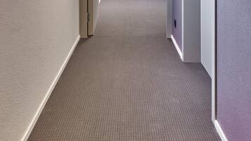 A hallway with carpeted floors, doors, and a fire extinguisher.