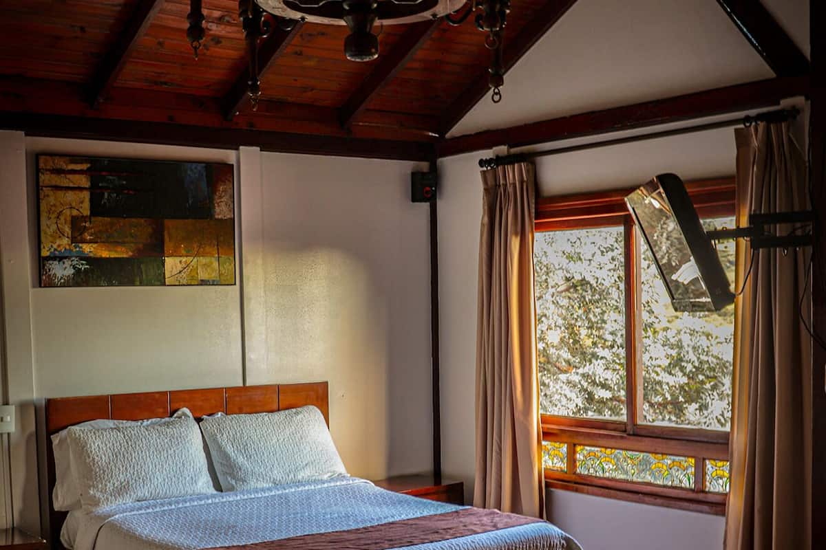 A wooden-framed bedroom with a bed, a window with curtains, and a chandelier.
