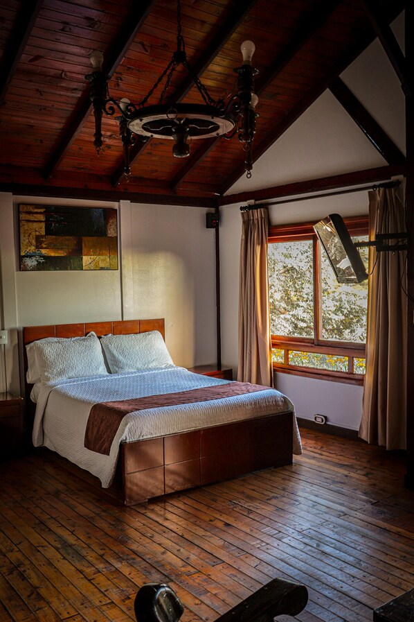 A wooden-framed bedroom with a bed, a window with curtains, and a chandelier.