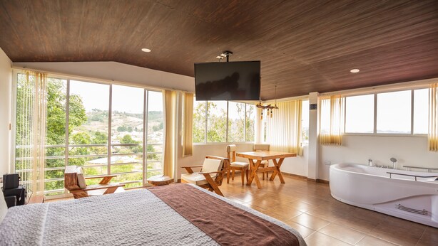 A spacious bedroom with a large bed, a wooden dining table, and a bathtub. - Hotel La Posada del Rancho (Popayán)