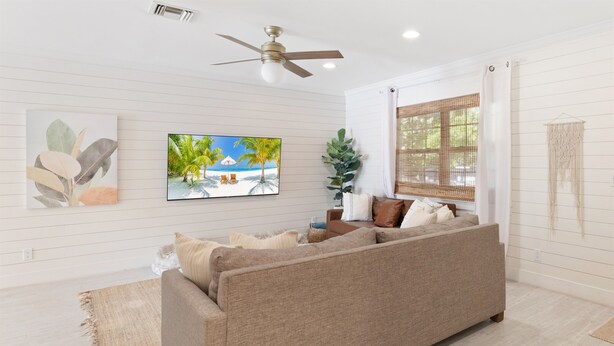 Una sala de estar con un sofá color beige, un ventilador de techo y dos cuadros colgados en la pared.