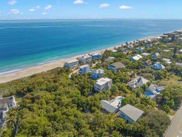 An aerial view of a coastal residential area with houses, a beach, and clear blue waters.