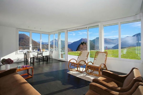 A spacious room with large windows, a dining area, and a seating area with wicker chairs.