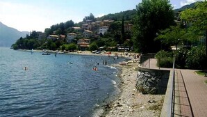 Una zona costera con playa, un muro de piedra y edificios al fondo.