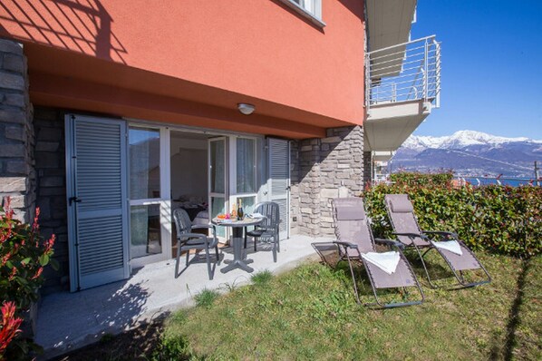 A two-story building with a stone facade, a balcony with a metal railing, and a patio area with outdoor furniture.
