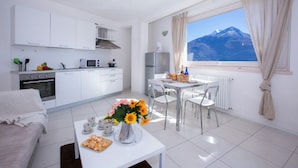Una cocina moderna con armarios blancos, un comedor con mesa y sillas, y un ventanal con vistas a la montaña.