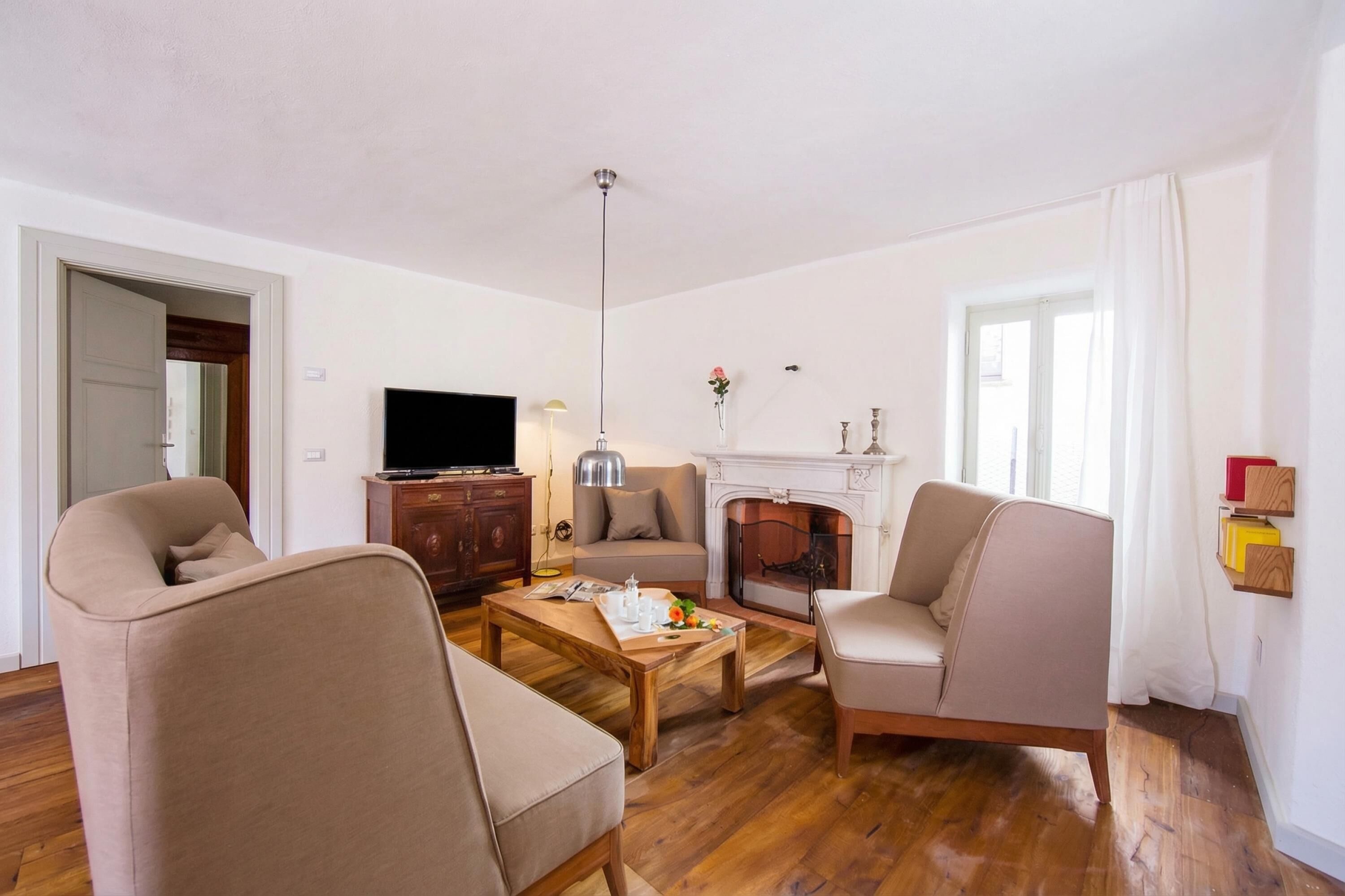 A living room with a sofa, armchair, wooden coffee table, fireplace, television, and a door.