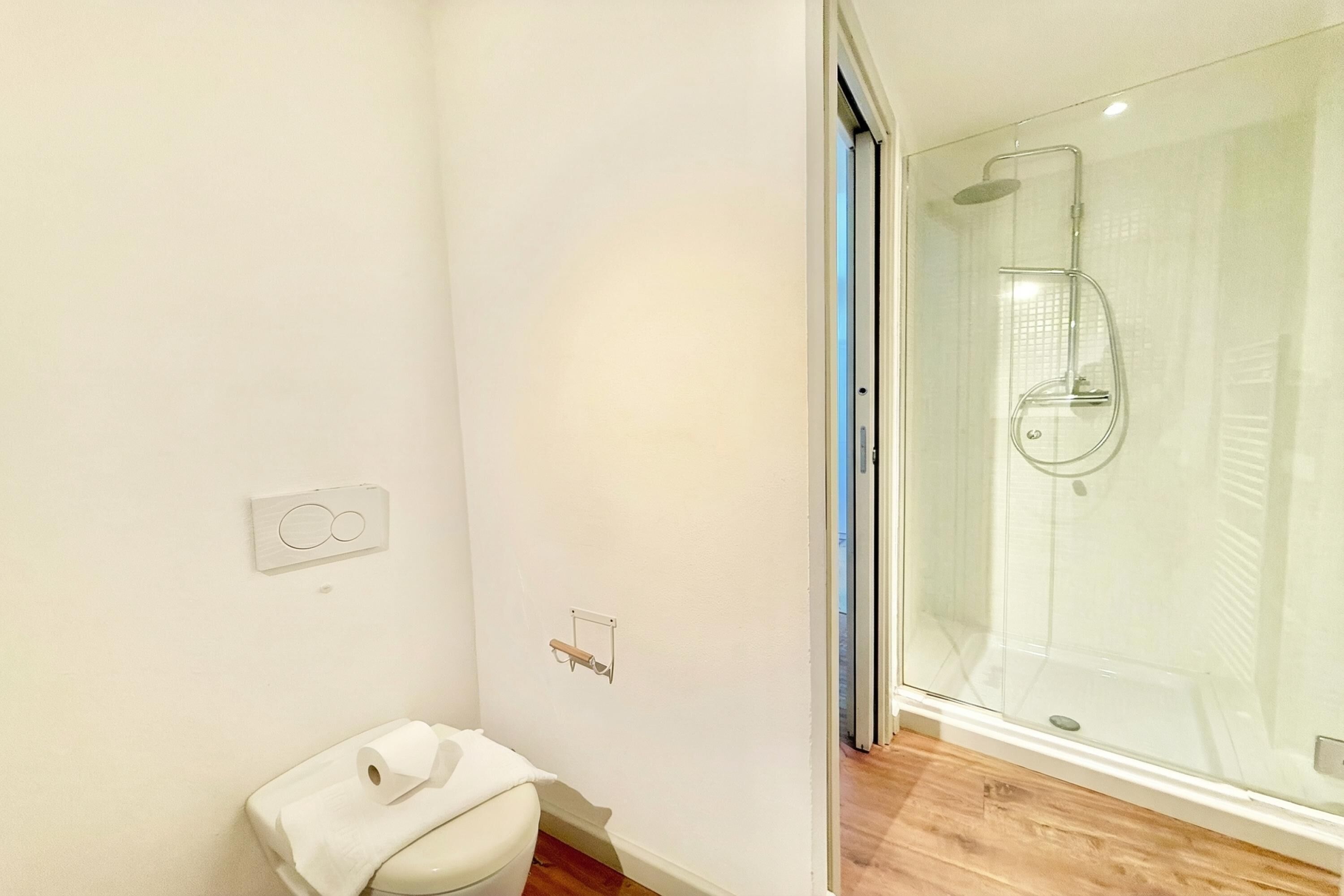 Et moderne badeværelse med toilet, brusekabine i glas og trægulv.