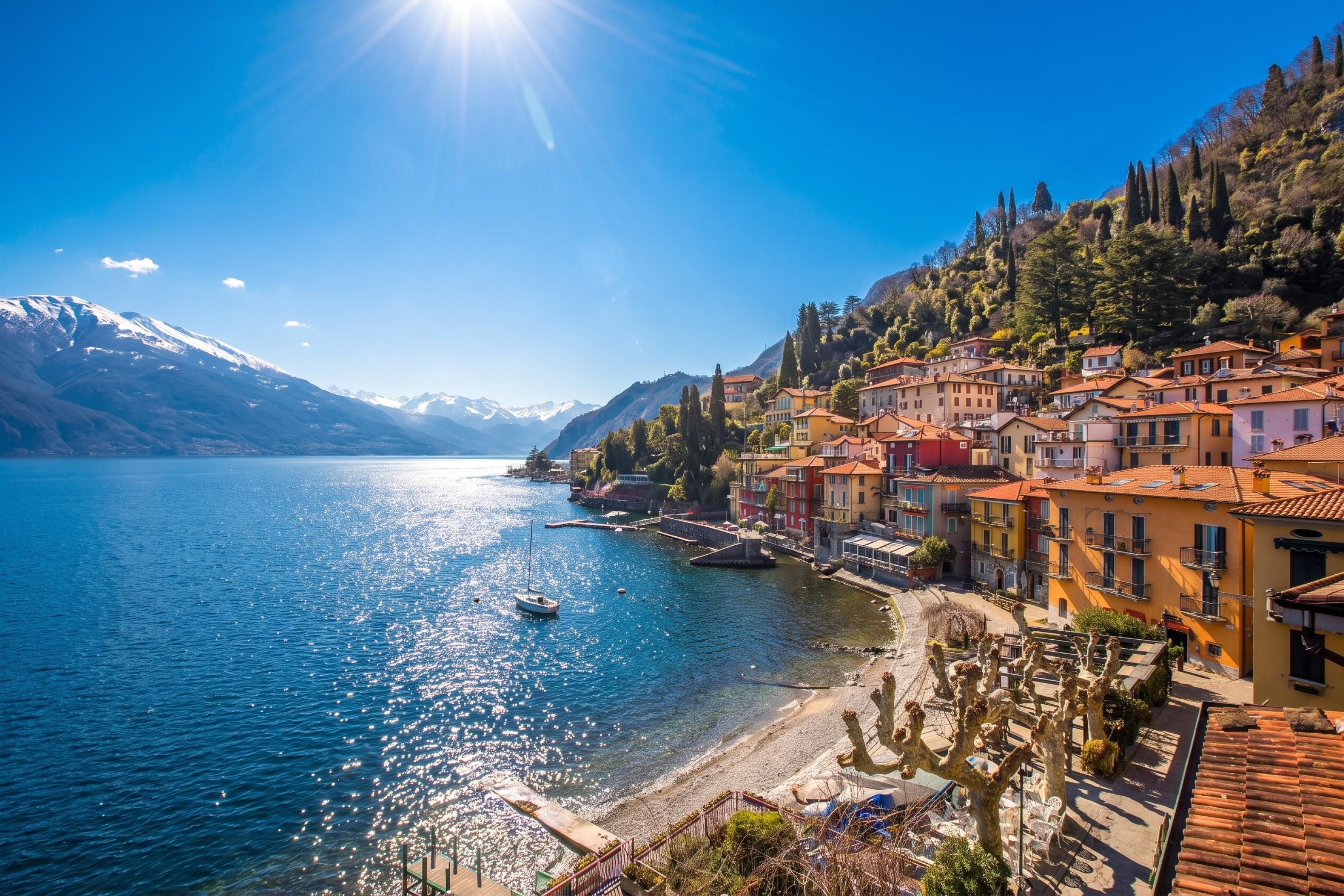 Uma cidade às margens de um lago, com edifícios ao longo da costa, um barco na água e montanhas ao fundo.
