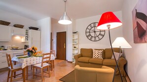 Ein Wohnzimmer mit einer Couch, einem Esstisch mit Stühlen, einer Küchenzeile und einer Uhr an der Wand.