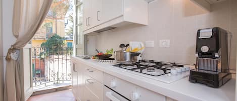 A kitchen with white cabinets, a gas stove, a coffee machine, and a view of the outside.