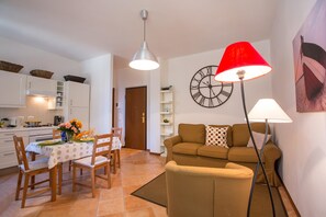 Un salon avec un canapé, une table à manger avec des chaises, un coin cuisine et une horloge au mur.