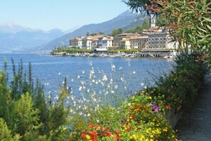 A lakeside town with buildings along the shore, a clear sky, and mountains in the background. - Bellagio Spiaggia Due (Bellagio)