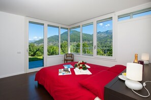 A bedroom with a large bed, a nightstand, a lamp, and a view of mountains.