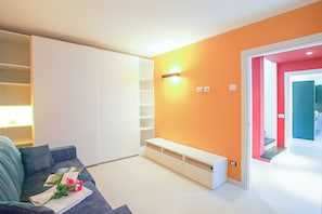 A modern living room with a sofa, a white entertainment unit, and a bright orange accent wall. - Villa Intelvi (Cerano d'Intelvi)