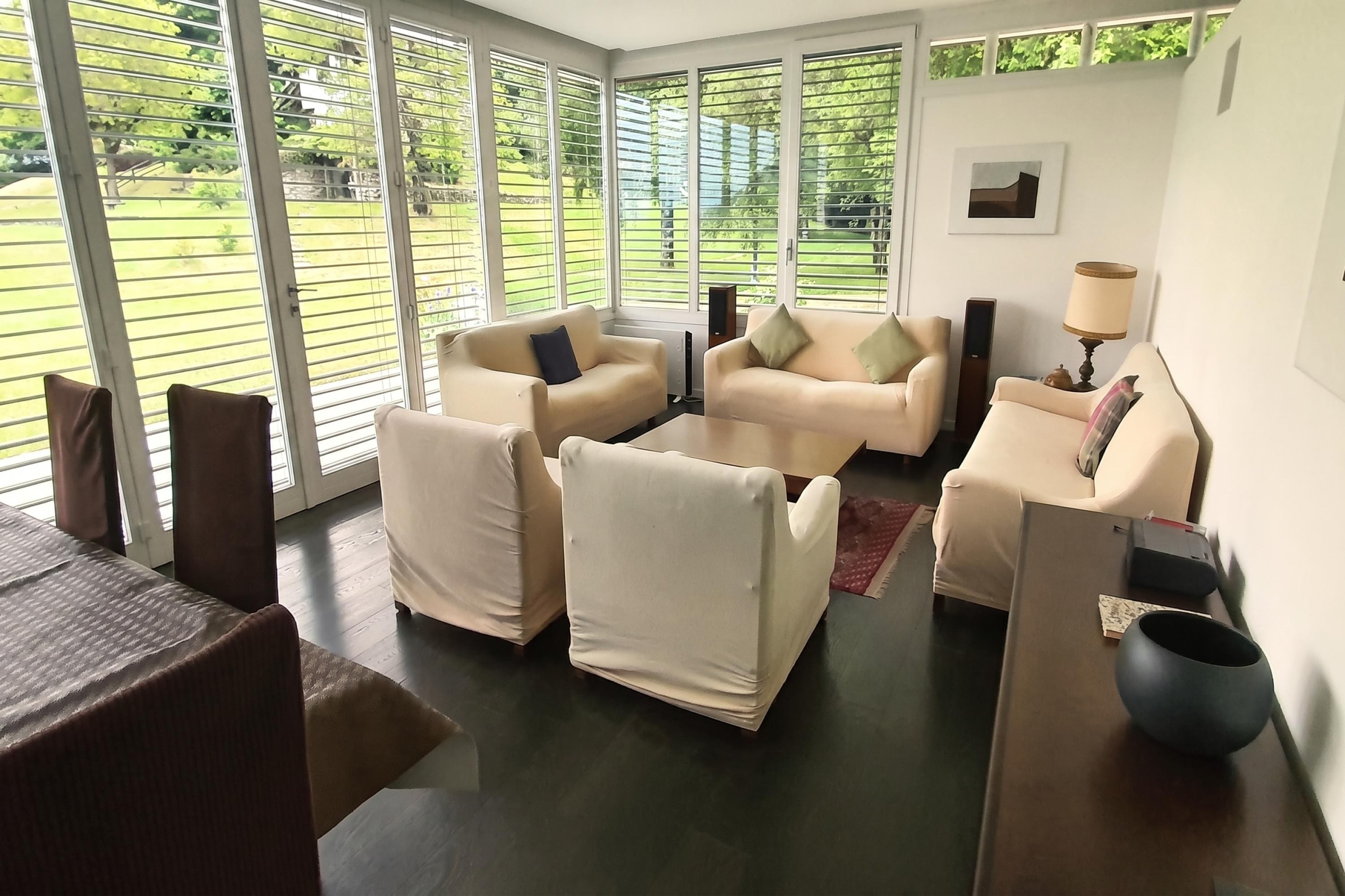 Ein modernes Wohnzimmer mit großem Fenster, einer Sofagarnitur, einem Couchtisch und einer Lampe.